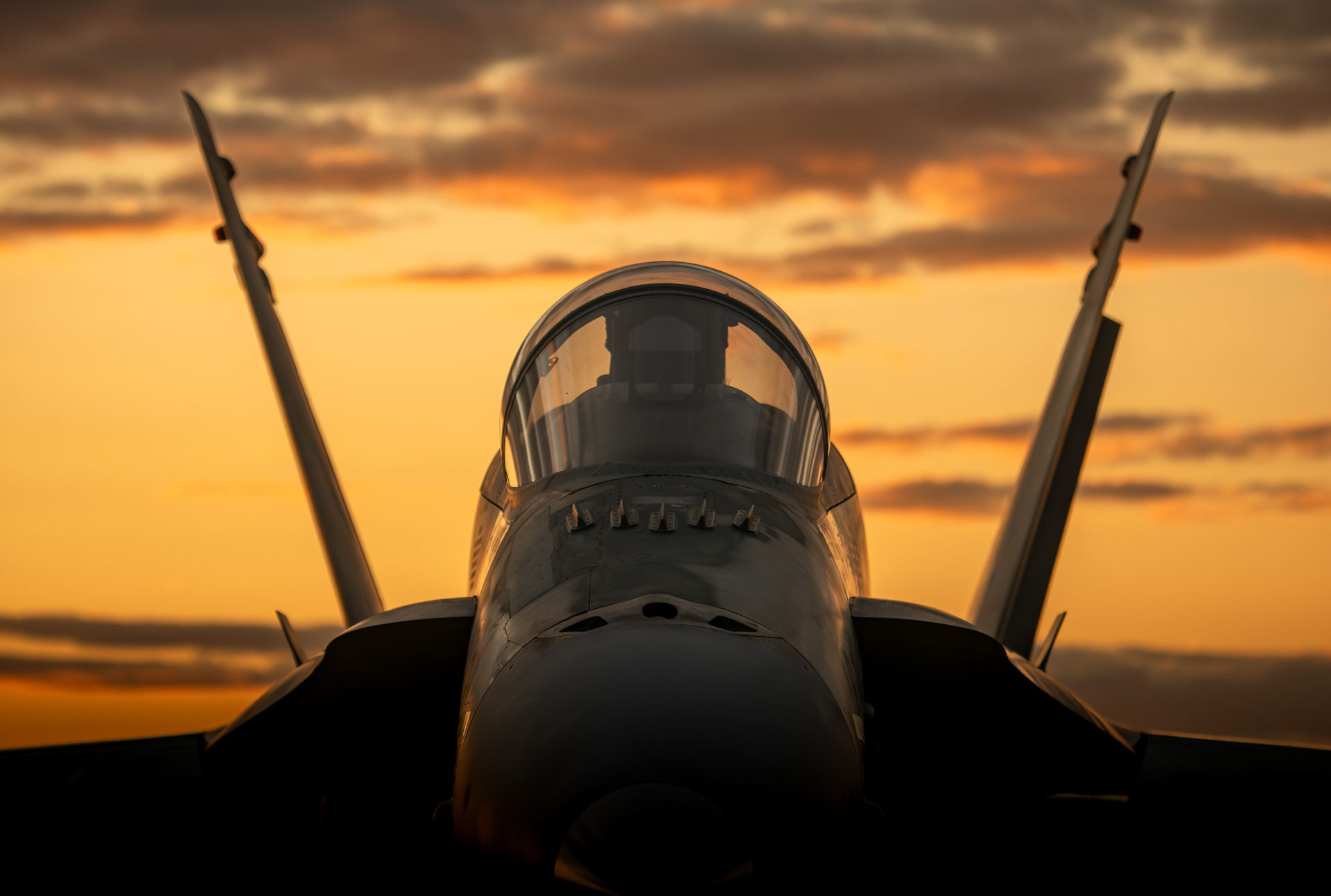 Fighter jet canopy and tail fins against sunset sky